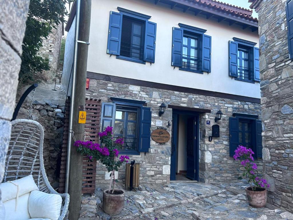 SokeDomatia Stone Hotel的一座石头房子,拥有蓝色的窗户和紫色的鲜花