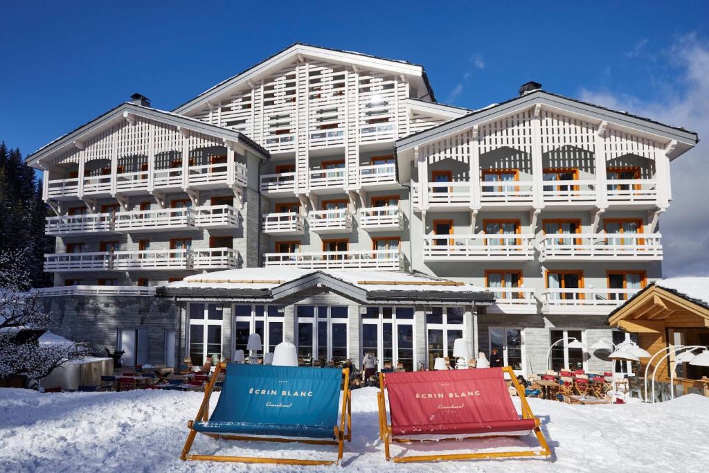谷雪维尔Ecrin Blanc Resort Courchevel的雪中的酒店,前面有两把椅子