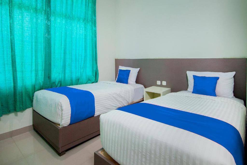 PangururanHotel Wisata Samosir By Helocus的两张位于酒店客房的床,配有蓝色窗帘