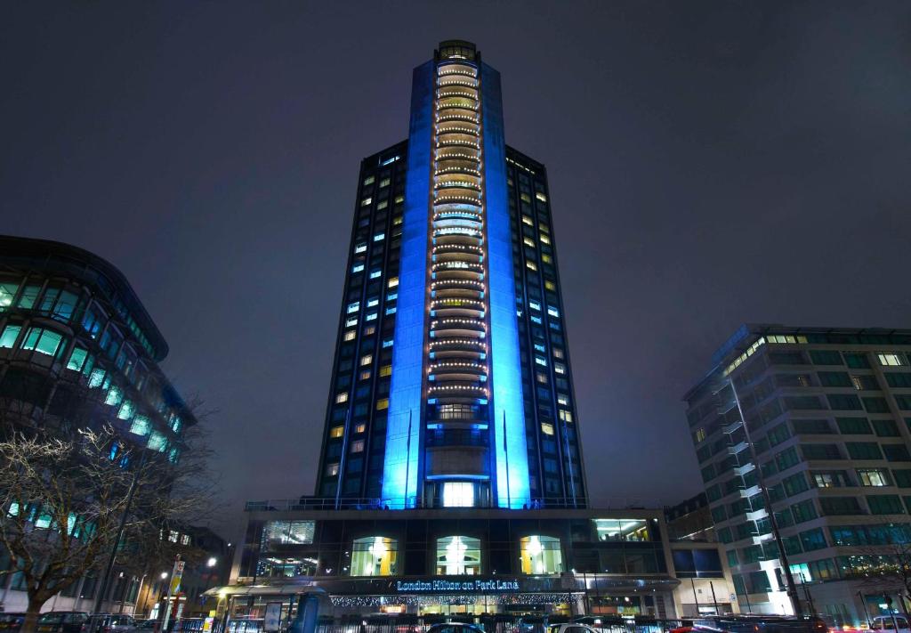 伦敦伦敦希尔顿花园弄酒店的一座高大的建筑,晚上有蓝色的灯光