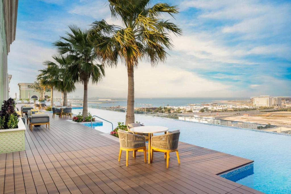 多哈The Plaza Doha, LXR Hotels & Resorts的一个带桌椅的阳台和一个游泳池