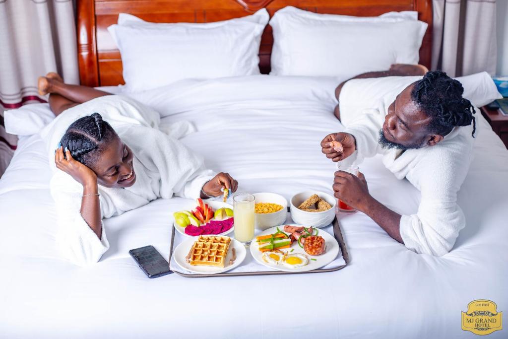 东勒贡MJ Grand Hotel的男人和女人躺在床上,放着一盘食物