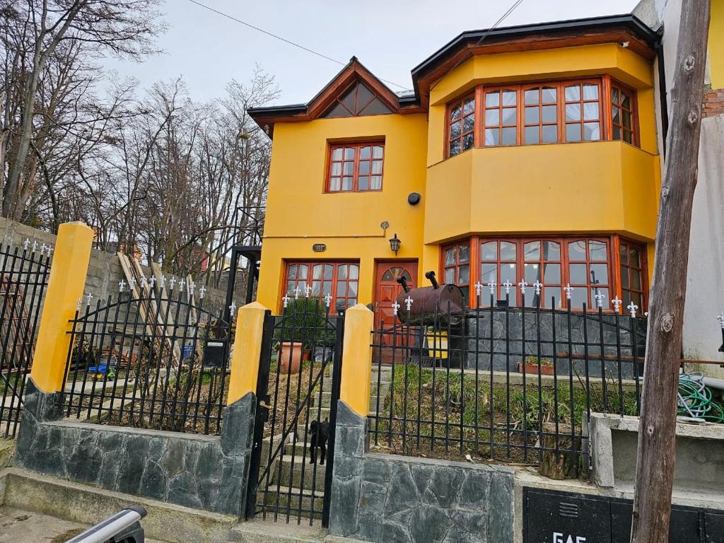 乌斯怀亚La Herradura de Ushuaia的黄色的房子,有红色的窗户和栅栏
