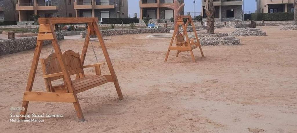 艾因苏赫纳شاليه بالعين السخنة的两只木秋千坐在建筑物前的沙子上