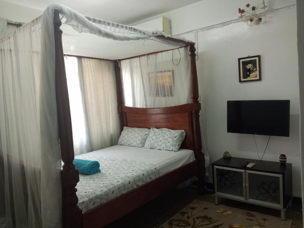 蒙巴萨Paradise Apartment的一间卧室配有一张天蓬床和一台电视机