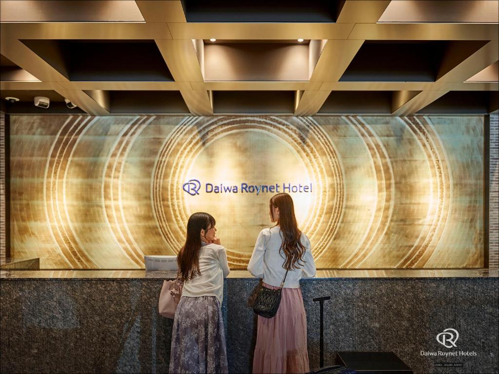 京都京都四条乌丸大和ROYNET酒店的两个妇女站在墙上,有标志