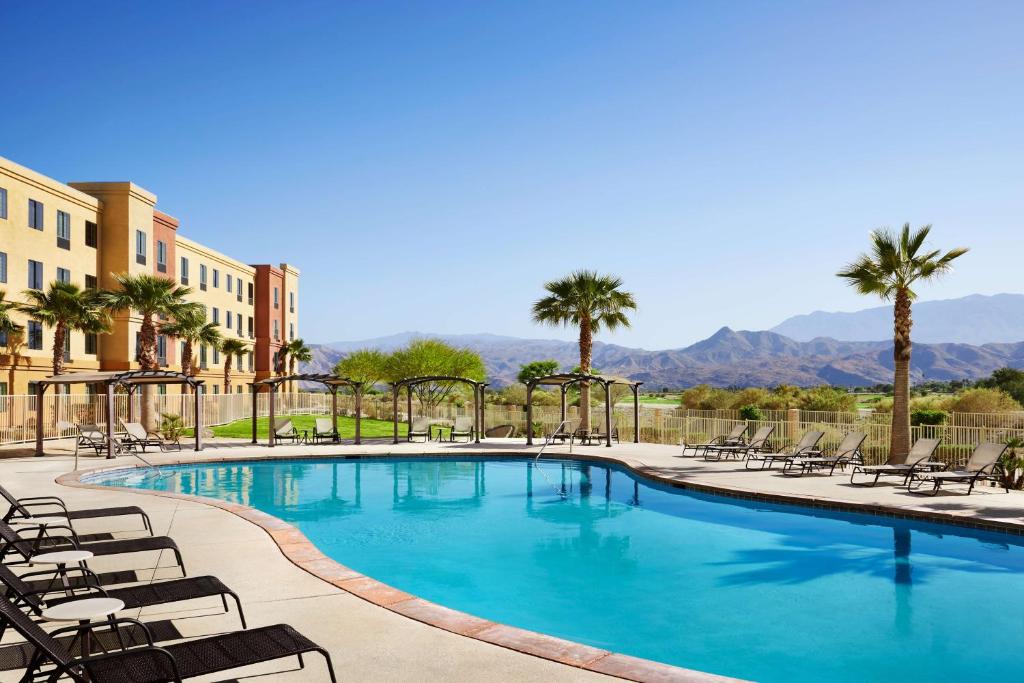 大教堂城Homewood Suites by Hilton Cathedral City Palm Springs的一个带椅子和棕榈树的大型游泳池