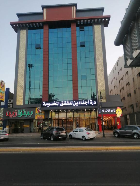 泰布克درة اجنادين للشقق المخدومة的一座大型建筑,前面有汽车停放