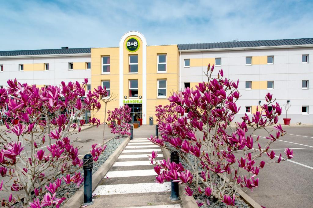 绍莱B&B HOTEL Cholet Nord的停车场前方有粉红色花的建筑
