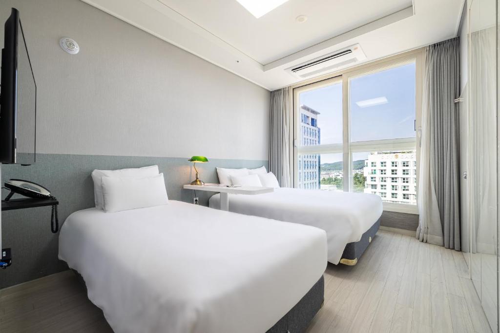 仁川市GL City Hotel Incheon Airport的配有窗户的酒店客房内的两张床