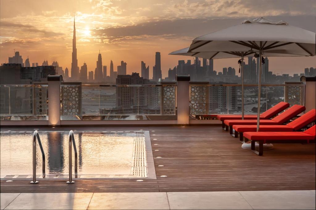 迪拜DoubleTree by Hilton Dubai Al Jadaf的一个带椅子和遮阳伞的屋顶甲板,一个城市