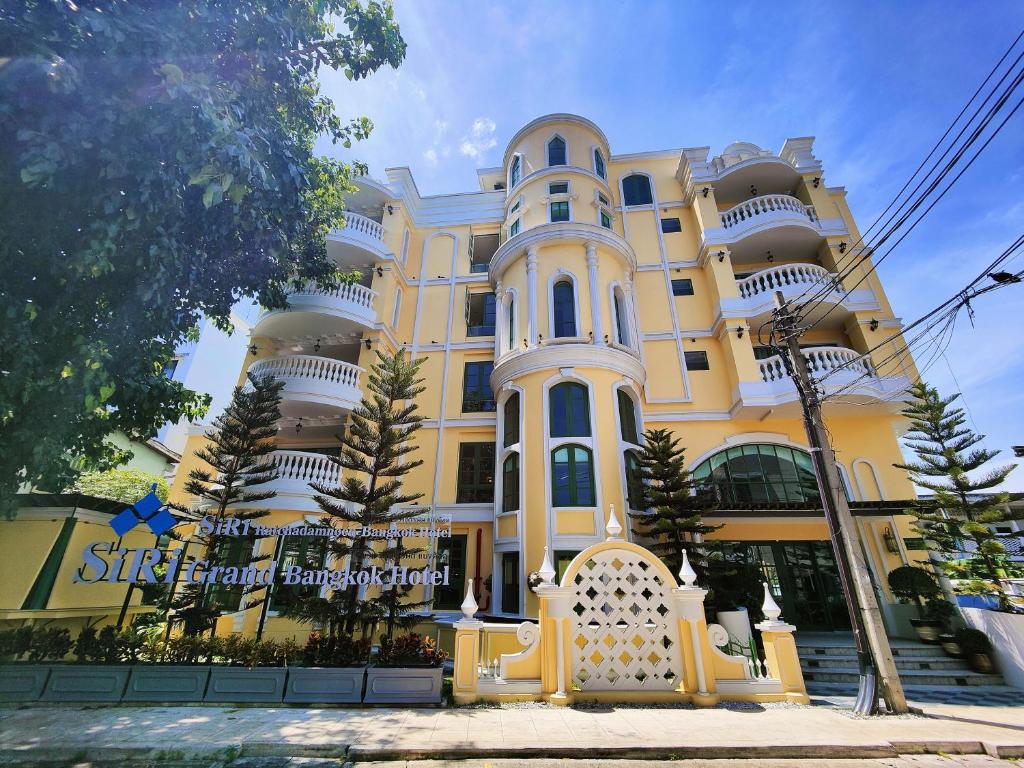 曼谷Siri Ratchadamnoen Bangkok Hotel的一座黄色和白色的大建筑,前面有树木