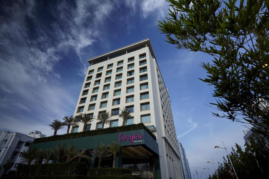 钦奈钦奈图尔亚 - OMR IT高速公路酒店的一座高大的白色建筑,前面有棕榈树