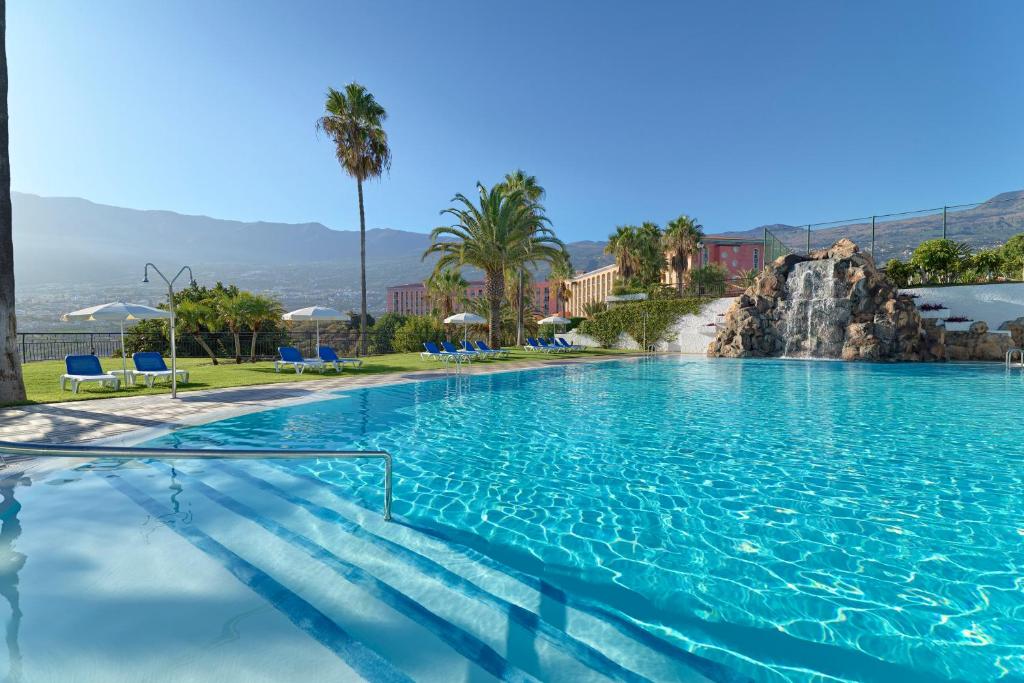 拉克鲁斯Hotel Las Águilas Tenerife, Affiliated by Meliá的一个带蓝色椅子和棕榈树的大型游泳池