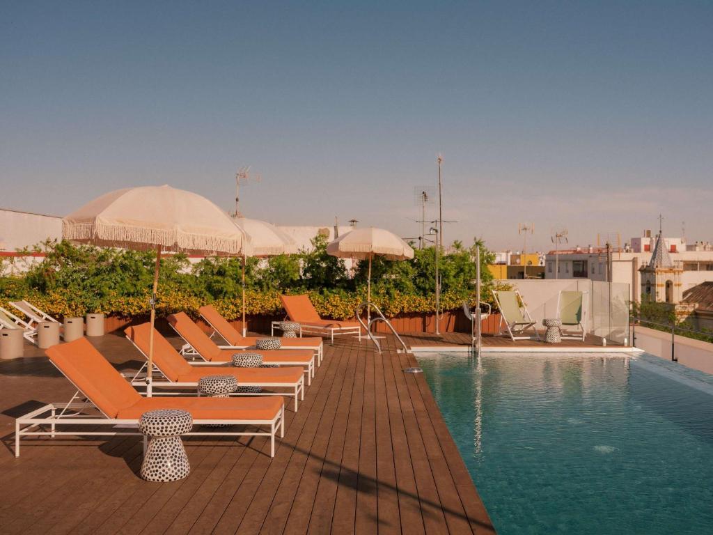 塞维利亚Ibis Styles Sevilla City Santa Justa的大楼内带躺椅和遮阳伞的游泳池