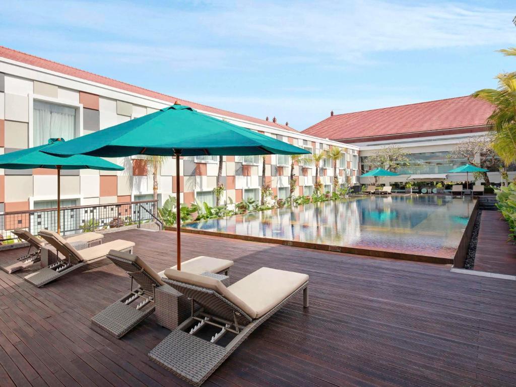 库塔巴厘岛国际机场诺富特酒店的一个带游泳池、椅子和遮阳伞的酒店