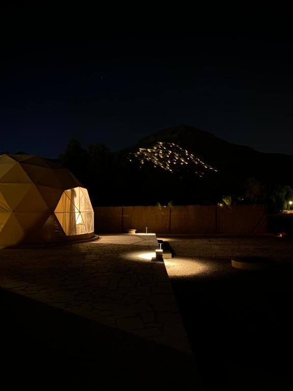 Al Fawwāzمنتجع جلامبنغ - Glamping Resort的夜晚有灯光的帐篷,背景是山