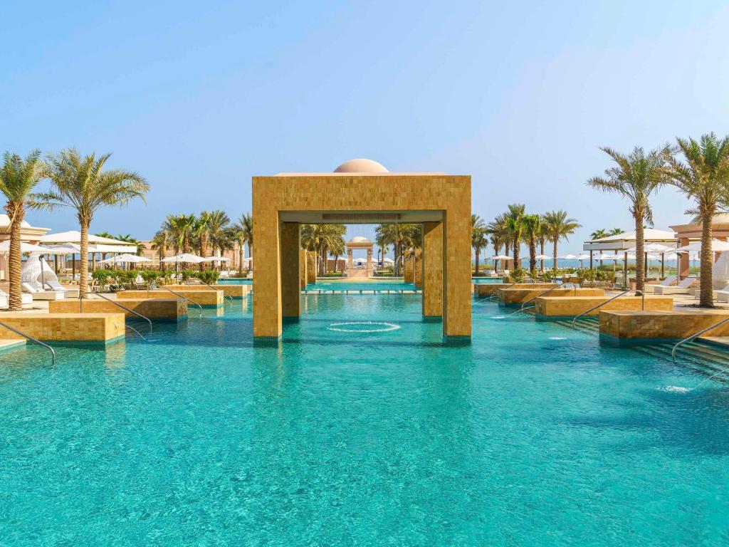 阿布扎比Rixos Marina Abu Dhabi的拥有蓝水和棕榈树的度假村的游泳池