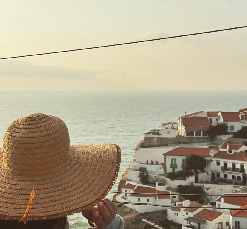 辛特拉Azenhas do Mar Cliffs House的戴着稻草帽,看着大海的人