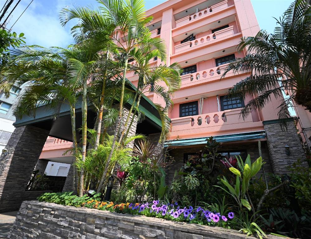 石垣岛ホテルアビアンパナ石垣島的一座粉红色的建筑,种植了棕榈树和鲜花