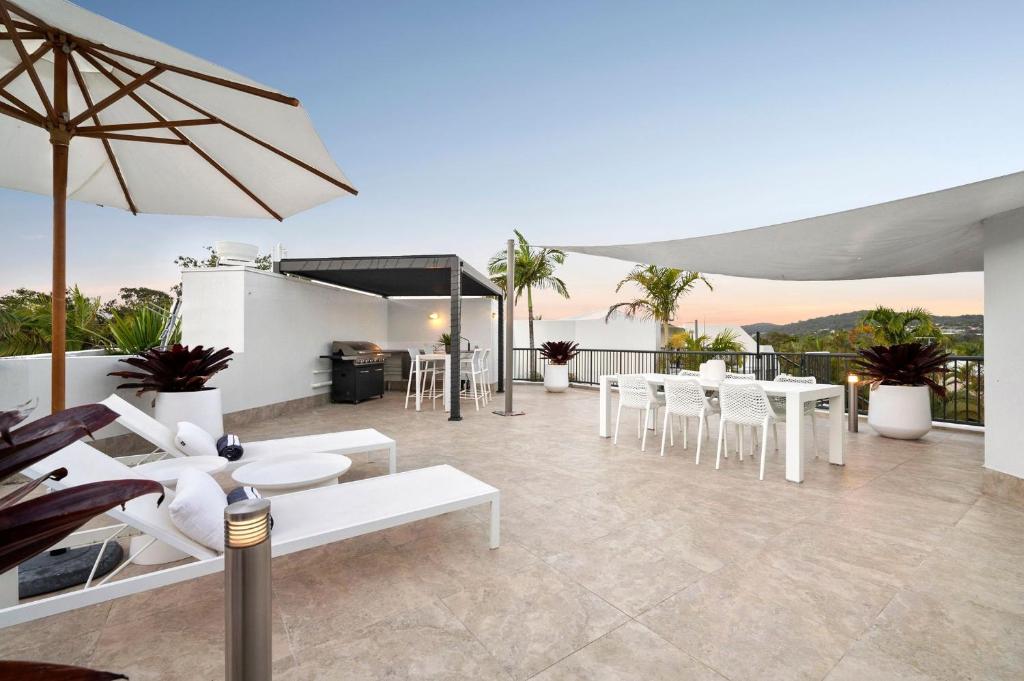 努萨角Penthouse with Private Roof top terrace- NOOSA的庭院配有白色的桌椅和遮阳伞。