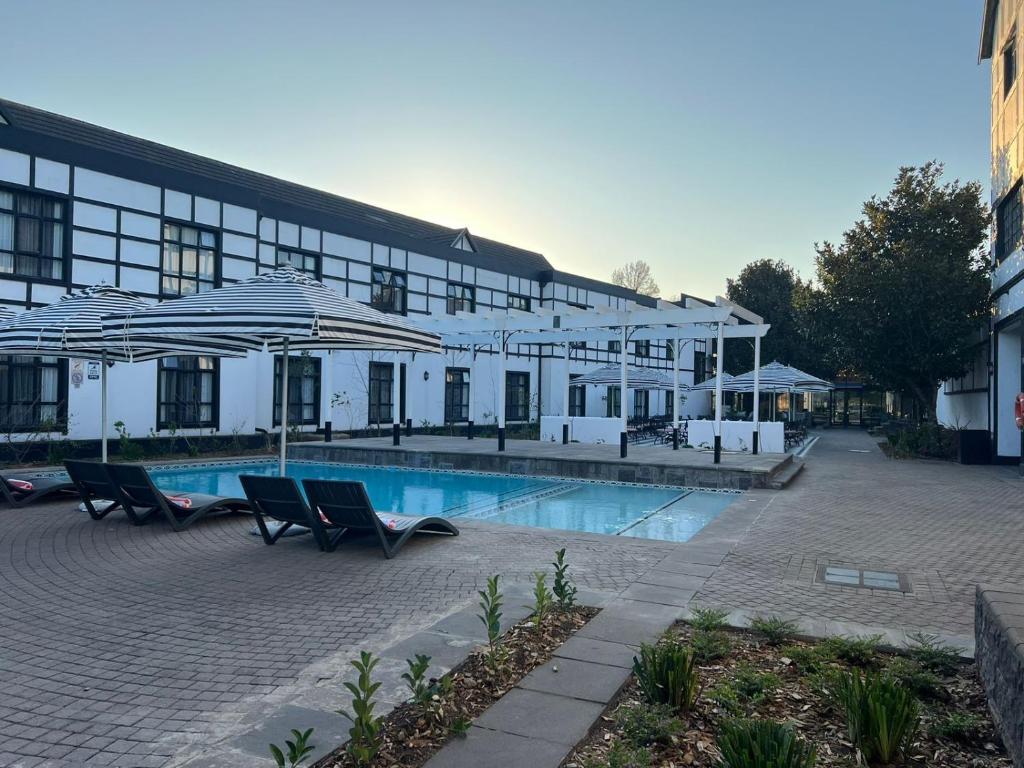 希尔顿ANEW Hotel Hilton Pietermaritzburg的一座带游泳池的大型建筑,游泳池配有遮阳伞