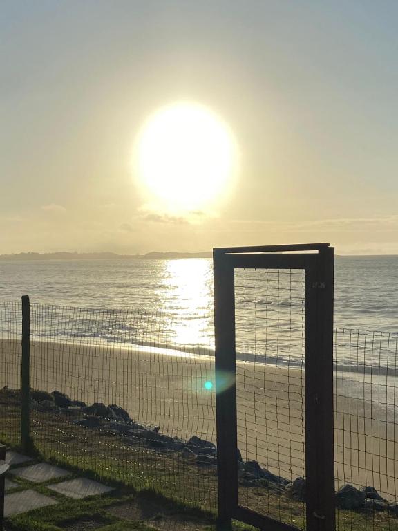 里约达欧特拉斯Casa de Praia PÉ NA AREIA em Rio das Ostras RJ的海滩上的栅栏,阳光在天空中