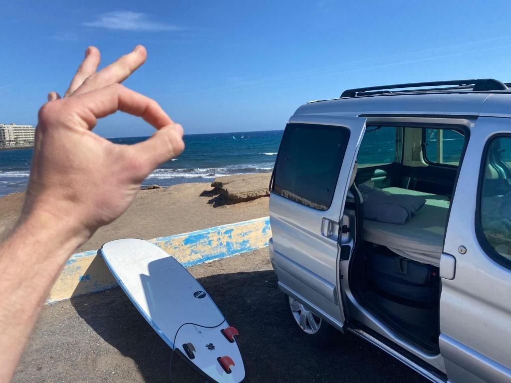 厄尔梅达诺CamperTF - old but lovable mini caravans in Tenerife的一辆面包车旁的冲浪板上打一个和平标志的人