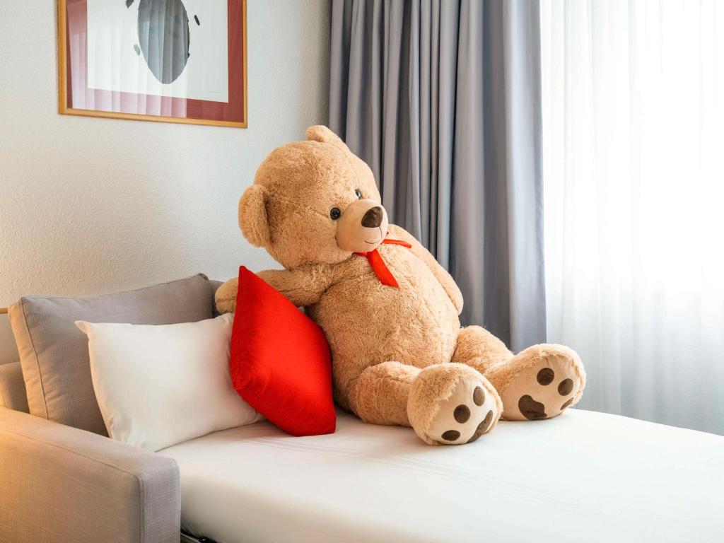 格拉斯哥诺富特格拉斯哥中心酒店的一只泰迪熊坐在床上,带红色枕头