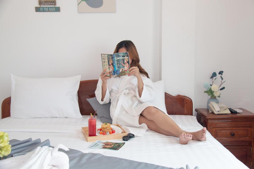 金边White Corner Hotel的坐在床上读杂志的女人