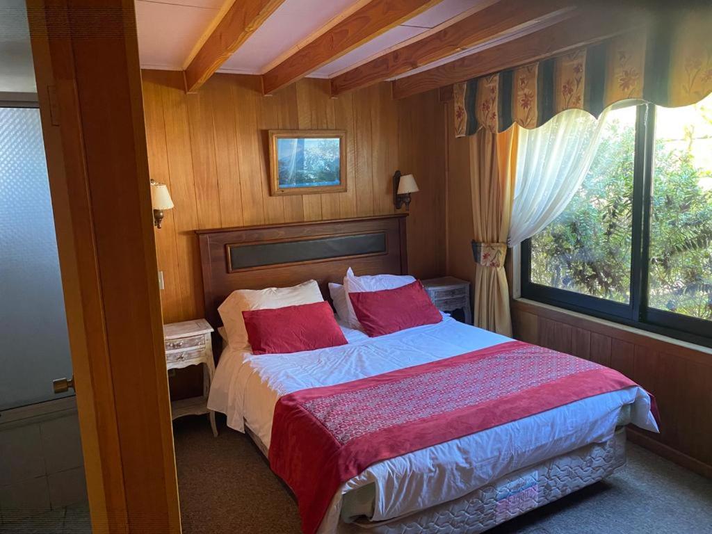 瓦尔迪维亚Hostal Buenaventura的一间卧室配有一张带红色枕头的床和一扇窗户