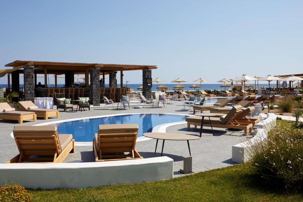 佩里沃罗Sea Breeze Santorini Beach Resort, Curio By Hilton的一个带桌椅的游泳池的度假酒店