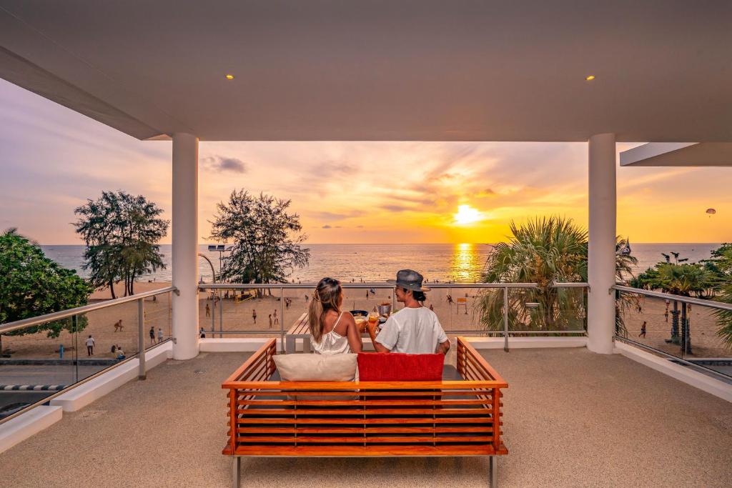 卡伦海滩Paradox Resort Phuket - SHA Plus的坐在长凳上的男人和女人,看着日落