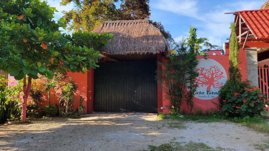 巴卡拉尔Casa Coral的一座红色的建筑,有一个黑色的车库,有草屋顶