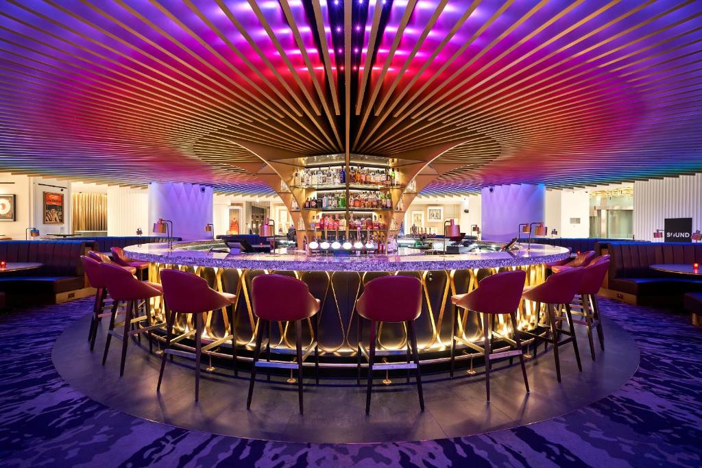 伦敦The Cumberland, London的一间酒吧,配有红色椅子和紫色照明