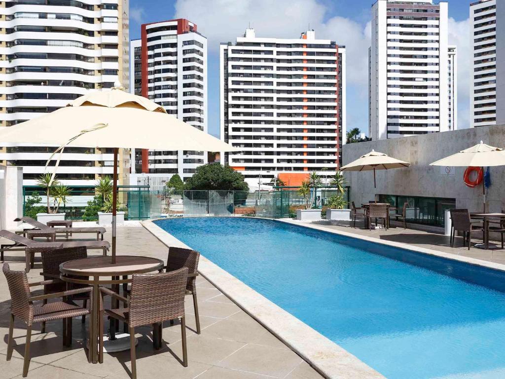 萨尔瓦多美琪尔萨尔瓦多皮图巴酒店的一座带桌椅的游泳池以及大楼
