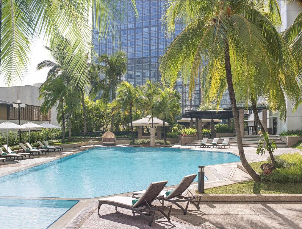 马尼拉马尼拉新世界酒店的一座带椅子和棕榈树的游泳池以及一座建筑