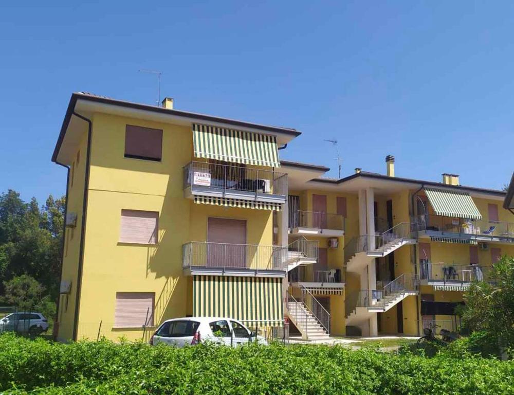 罗索利纳马雷Apartment Rosolina Mare 5的一座黄色的建筑,前面有一辆汽车