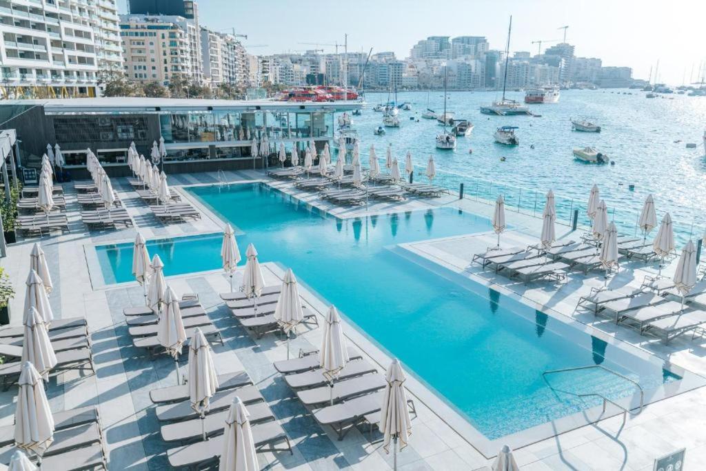 Il- GżiraValletta view Apartments by ST Hotels的水中带白色椅子和船只的游泳池