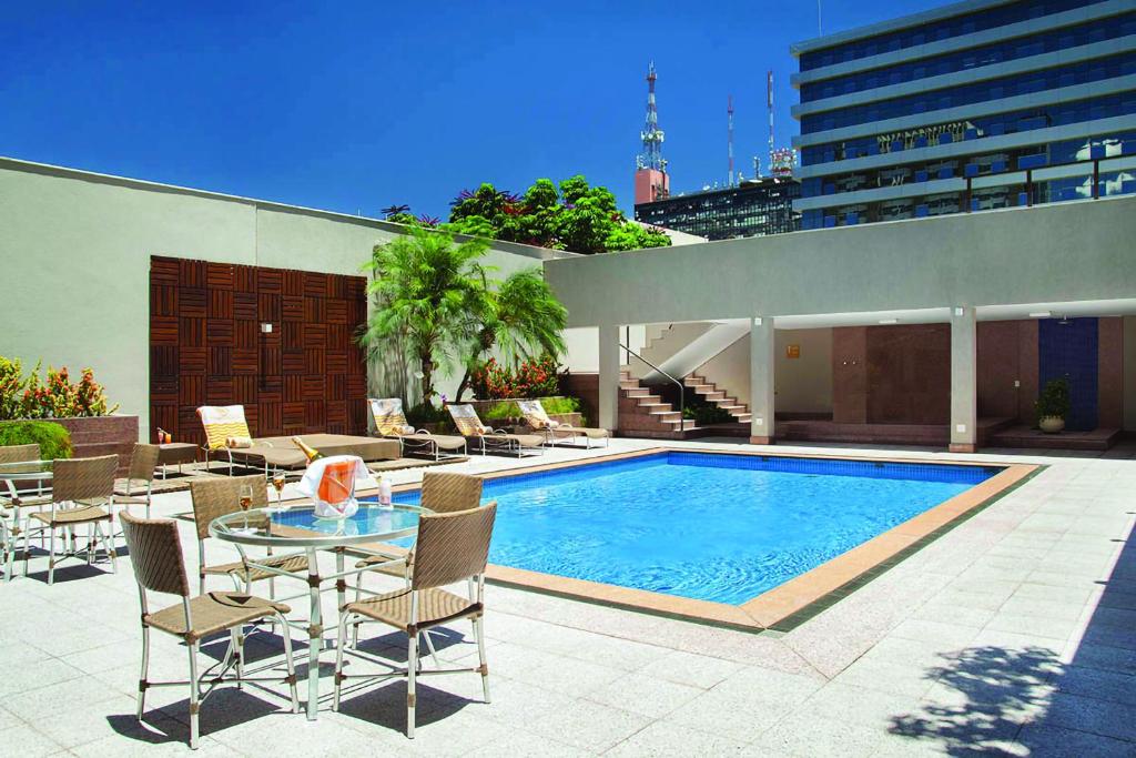 巴西利亚Windsor Plaza Brasilia的庭院设有游泳池、桌子和椅子。