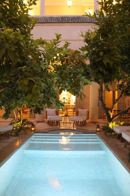 马拉喀什安贝瑞扎哈里摩洛哥传统庭院住宅的庭院内的游泳池,庭院里种有树木和椅子