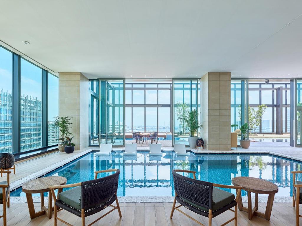 横滨Mitsui Garden Hotel Yokohama Minatomirai Premier的酒店游泳池设有桌椅和窗户。