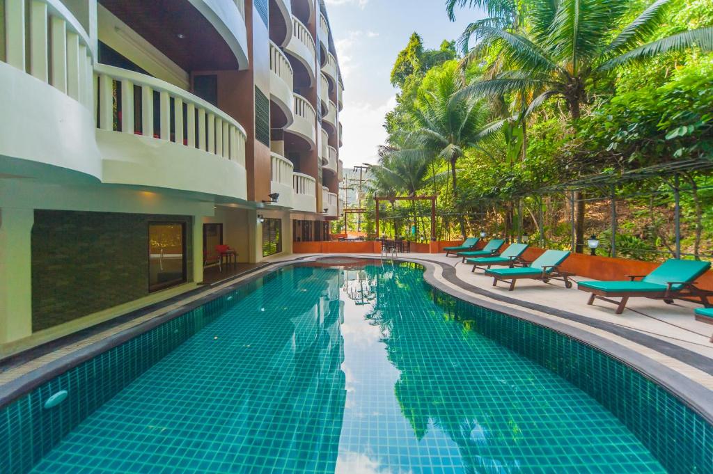 芭东海滩Ratana Hill Patong的一座游泳池,位于一座带椅子和树木的建筑旁边