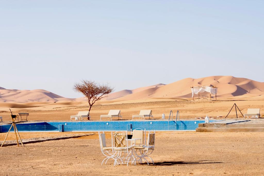 梅尔祖卡Sahara Royal Resort的沙漠中的游泳池,以沙丘为背景