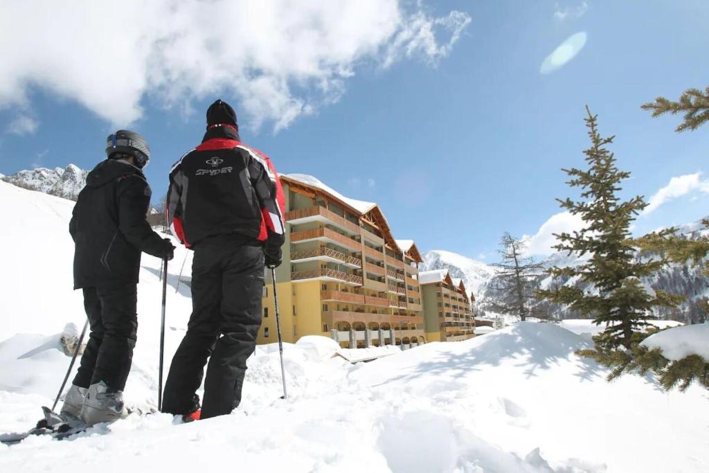 伊索拉Résidence Les Terrasses d'Isola 2000的两个人在酒店门前的雪地滑雪
