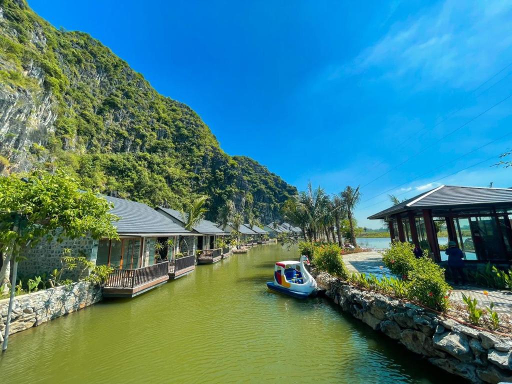 宁平Athena Premier Resort Ninh Bình的一条小船在房子旁边的河流里