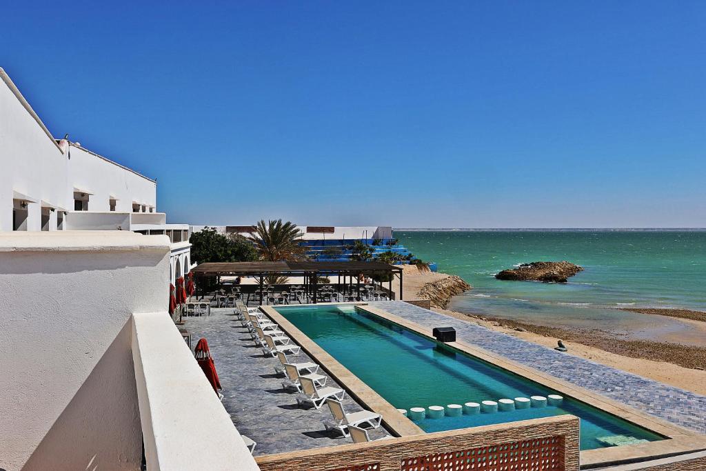 达赫拉Hôtel Calipau Riad Maison d'Hôtes的毗邻大海的游泳池,位于大楼旁