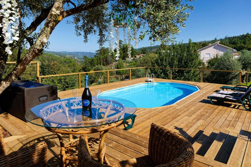 曼瓜尔迪Quinta Refúgios do Rio Dão的一个带游泳池的甲板上的一张桌子和一瓶葡萄酒