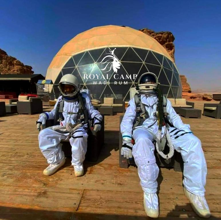 瓦迪拉姆ROYAl WADI RUM CAMP的两人坐在建筑物前的太空服上