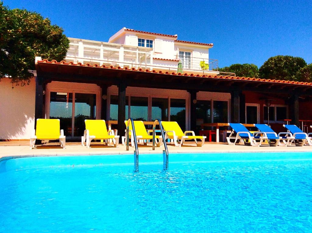 佩尼契FreeSurfCamp & Hostel的一个带黄色和蓝色椅子的游泳池以及一座房子